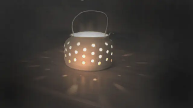 A lit candle pot with a wire handle