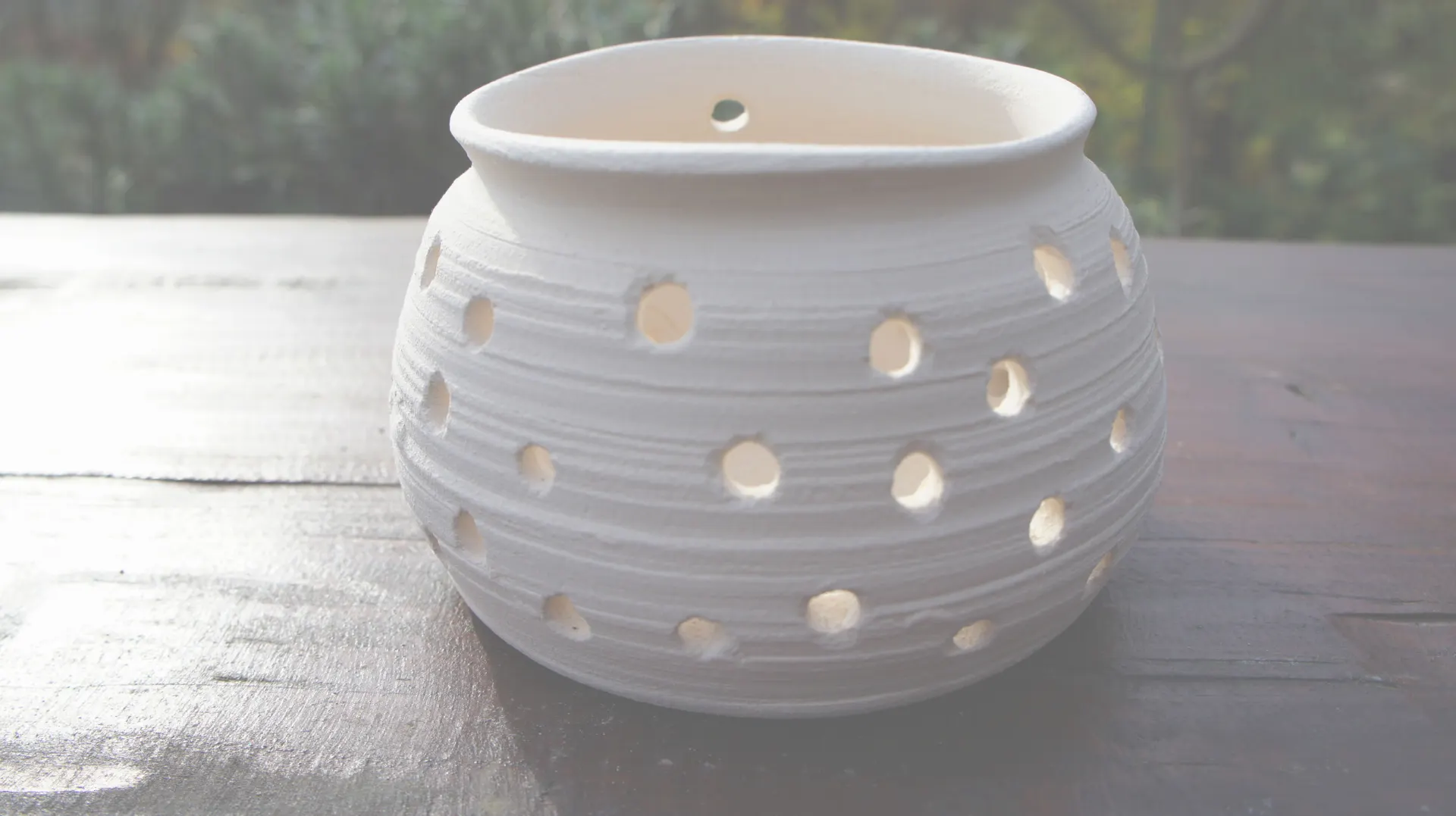 A white pot with holes on a garden table